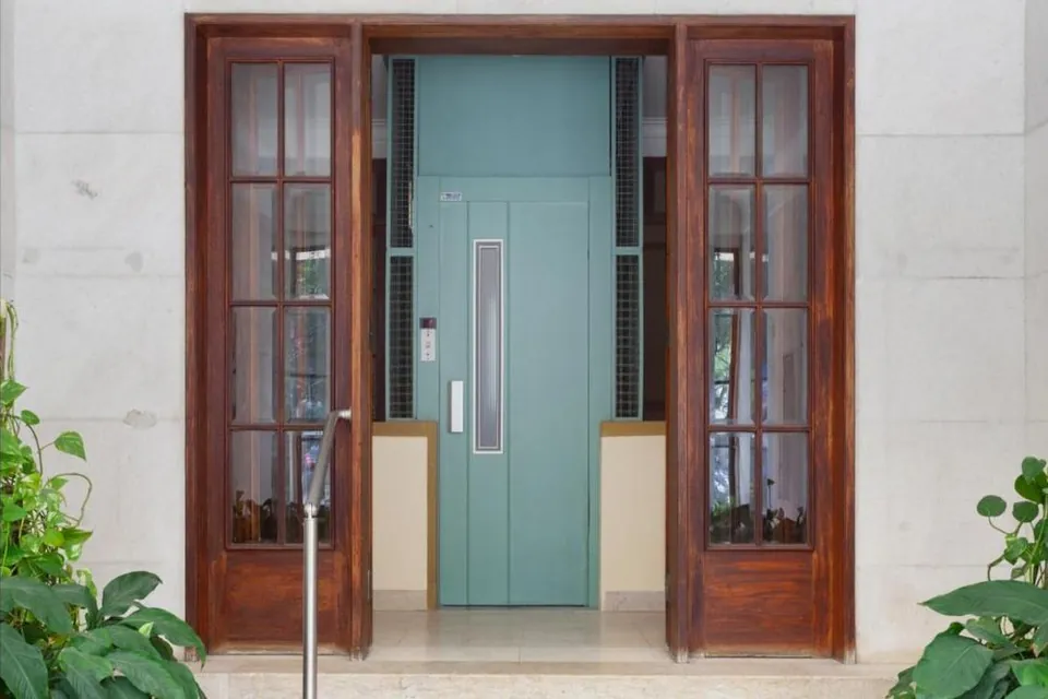 Entrada de um prédio em Lisboa, com portas de madeira e elevador verde